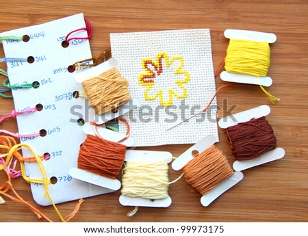 Cross-stitch set: colour palette, threads, canvas with a flower sewn against a wooden background