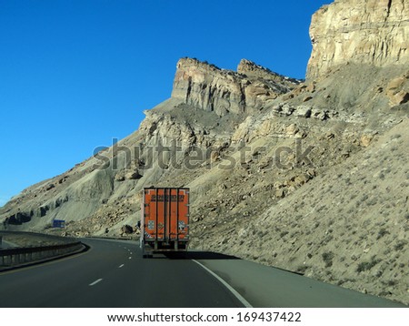 GRAND JUNCTION, COLORADO - JAN 28 - Orange semi truck drives past cliffs on Interstate I-70 near Grand Junction,  Colorado