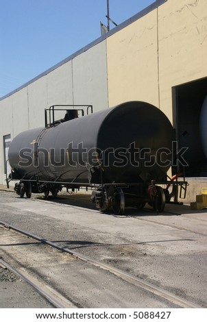 Black tank car, on railroad siding by pastel colored warehouse.		Seattle,	Pacific Northwest