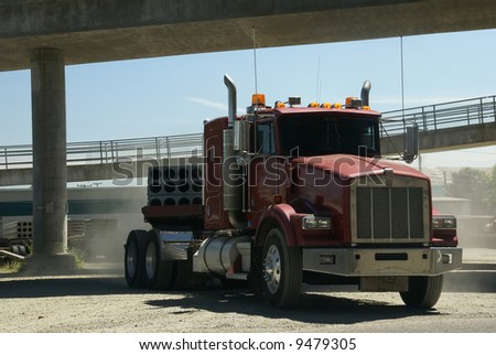 Red semi truck cab driving through dusty lot under freeway ramps,		Seattle,	Pacific Northwest