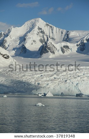Icebergs and snow covered mountain, with blue sky & Calm seas.  Petermann Island, Antarctica