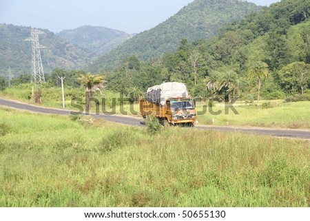 Brightly colored truck passes through rice paddies and jungle   in Orissa, India.