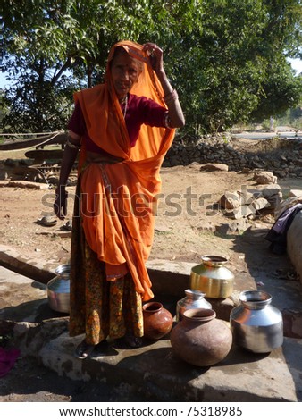 RAJASTHAN, INDIA - DEC 3 -Old Indian woman hauls water from well in metal pots,  on Dec 3, 2009, in Rajasthan, India