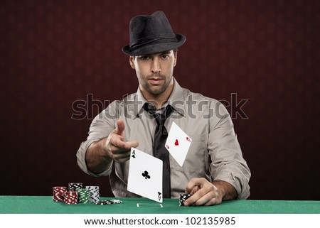 Poker player wearing hat, on a red background, throwing two ace cards.