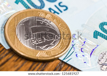 One Brazilian Real coin, over a 100 Real bill. Studio Shot.