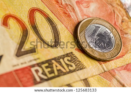 One Brazilian Real coin, over a 20 Real bill. Studio Shot.