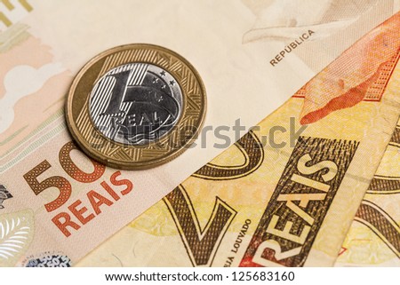 One Brazilian Real coin, over a 50 Real bill. Studio Shot.