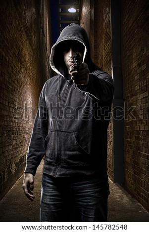 Thief in the hood pointing a gun, on a dark alley