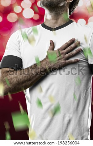 German soccer player, listening to the national anthem with his hand on his chest. On a red lights background.
