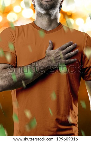 Dutchman soccer player, listening to the national anthem with his hand on his chest. On a orange lights background.