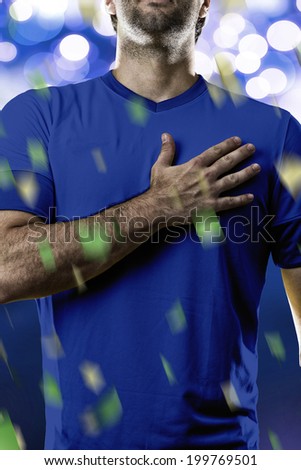 Italian soccer player, listening to the national anthem with his hand on his chest. On a blue lights background.