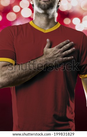 Spanish soccer player, listening to the national anthem with his hand on his chest. On a red lights background.