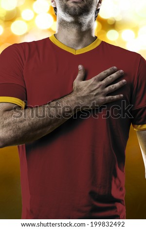Spanish soccer player, listening to the national anthem with his hand on his chest. On a yellow lights background.