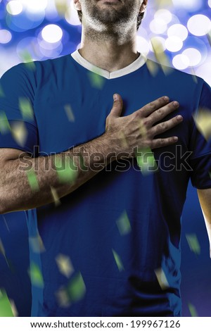 French soccer player, listening to the national anthem with his hand on his chest. On a blue lights background.