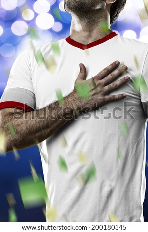 American soccer player, listening to the national anthem with his hand on his chest. On a blue lights background.