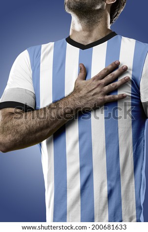 Argentinian soccer player, listening to the national anthem with his hand on his chest. On a blue background.