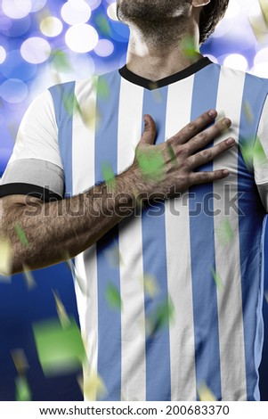 Argentinian soccer player, listening to the national anthem with his hand on his chest. On a blue lights background.