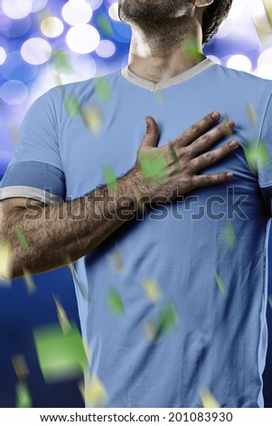 Uruguayan soccer player, listening to the national anthem with his hand on his chest. On a blue lights background.