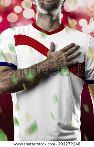 costa rican soccer player, listening to the national anthem with his hand on his chest. On a red lights background.
