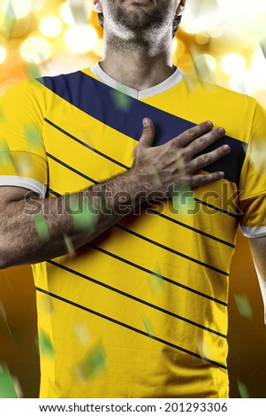 Colombian soccer player, listening to the national anthem with his hand on his chest. On a yellow lights background.