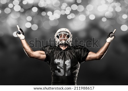 Football Player on a black uniform celebrating on a black lights background.
