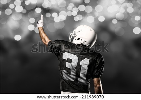 Football Player on a black uniform celebrating on a black lights background.
