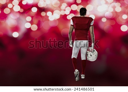 Football Player with a red uniform walking, showing his back on a red lights background.