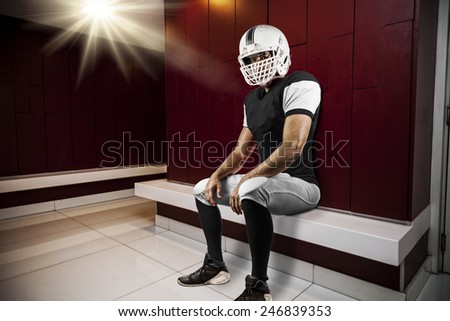 Football Player with a Black uniform seated in locker room.