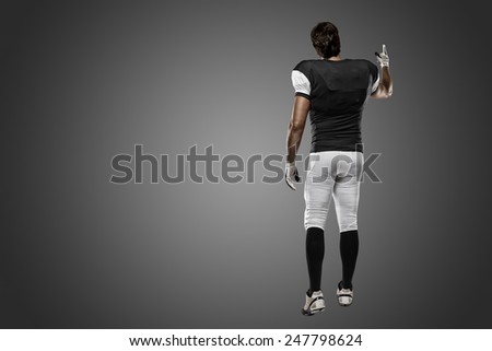 Football Player with a black uniform walking, showing his back on a black background.