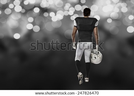Football Player with a black uniform walking, showing his back on a black lights background.
