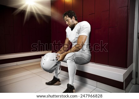 Football Player with a white uniform seated in locker room.