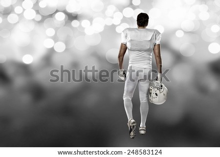 Football Player with a white uniform walking, showing his back on a white lights background.