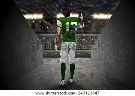 Football Player with a green uniform walking out of a Stadium tunnel.