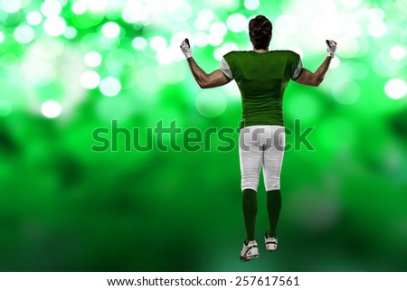 Football Player with a green uniform walking, showing his back on a green lights background.