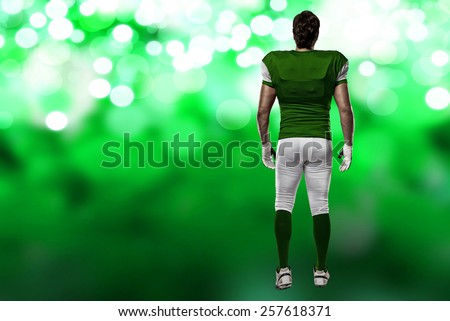 Football Player with a green uniform walking, showing his back on a green lights background.