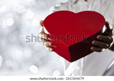 A Man holding a heart gift box in a gesture of giving in a silver lights background