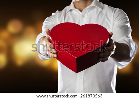 A Man holding a heart gift box in a gesture of giving in a yellow lights background