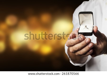 A Man holding a diamond ring in a yellow lights background.