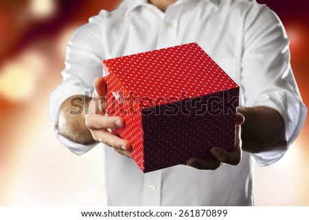 A Man holding a gift box in a gesture of giving in a orange lights background.