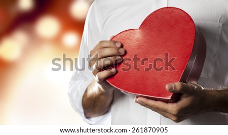 A Man holding a heart gift box in a gesture of giving in a orange lights background