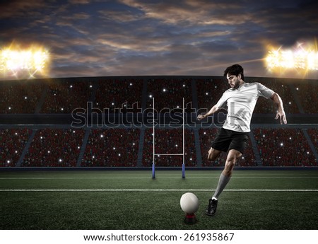 Rugby player in a white uniform kicking a ball on a stadium.