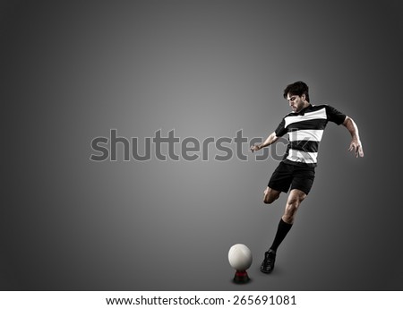 Rugby player in a black uniform kicking a ball on a black background.