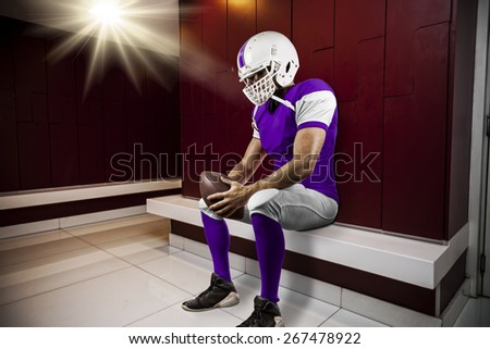 Football Player with a purple uniform seated in locker room.