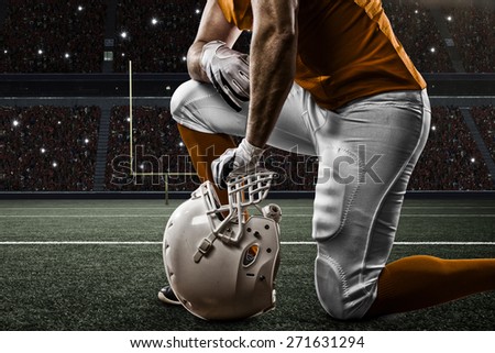 Football Player with a orange uniform on his knees, on a Stadium.