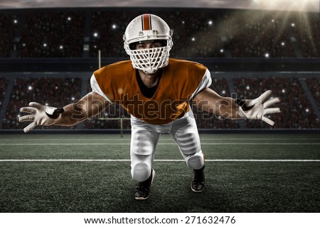 Football Player with a orange uniform making a tackle on a stadium.