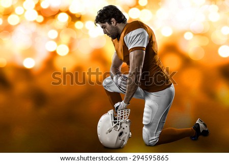 Football Player with a orange uniform on his knees, on a orange lights background.