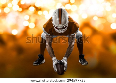 Football Player with a orange uniform on the scrimmage line, on a orange lights background.