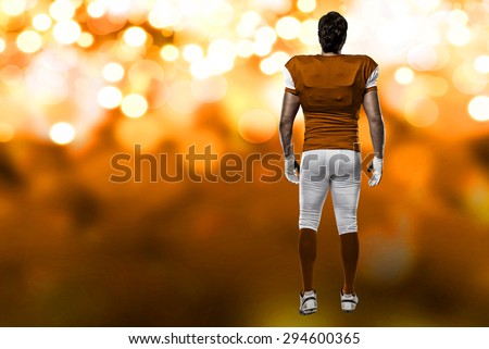 Football Player with a orange uniform walking, showing his back on a orange lights background.
