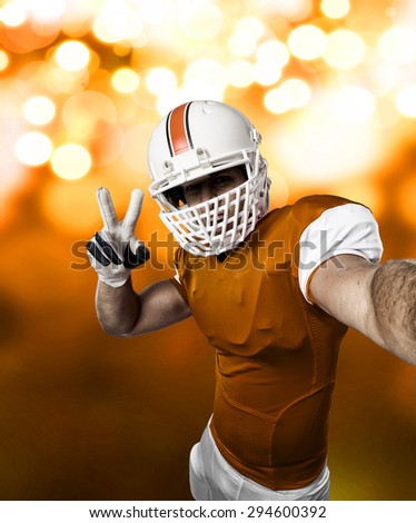 Football Player with a orange uniform making a selfie on a orange lights background.