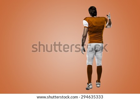 Football Player with a orange uniform walking, showing his back on a orange background.